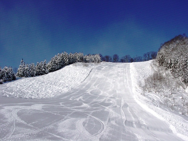 Asahi Shizen in Japan - a ski slope covered in snow under a blue sky.