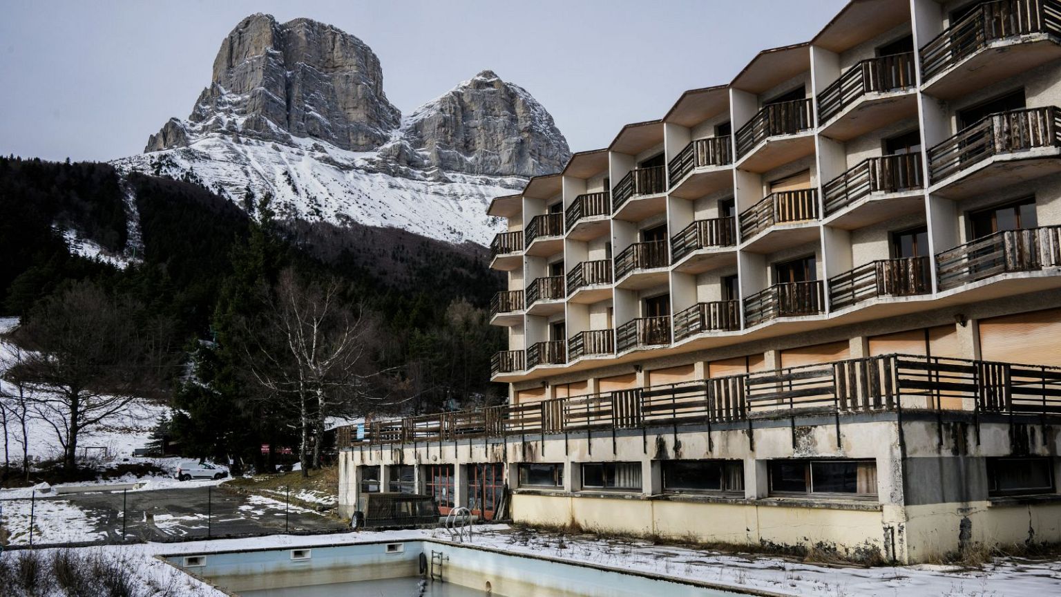 Col de l'Arzelier in France: a building with a pool in front of a snowy mountain.