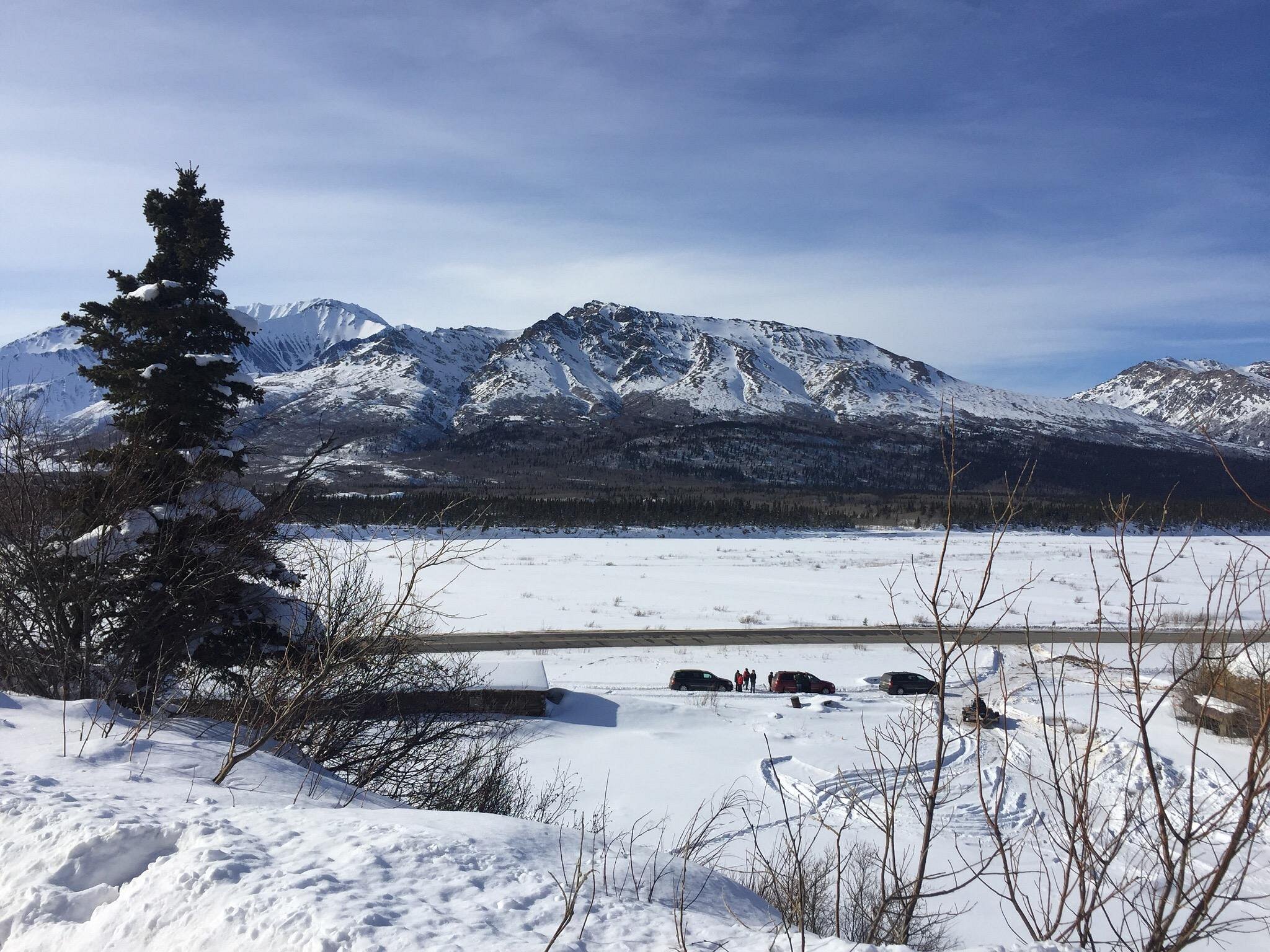 A lively winter sports scene captured at Black Rapid Alaska. The stunning snow-blanketed mountains provide a picturesque backdrop to the charming chalet. Chills of winter and adventure fill the air.