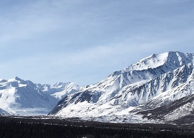Stunning winter scene at Black Rapid in Alaska featuring a significant mountain covered in snow. Nearby a chalet nestled in the snow implies a nearby ski resort.