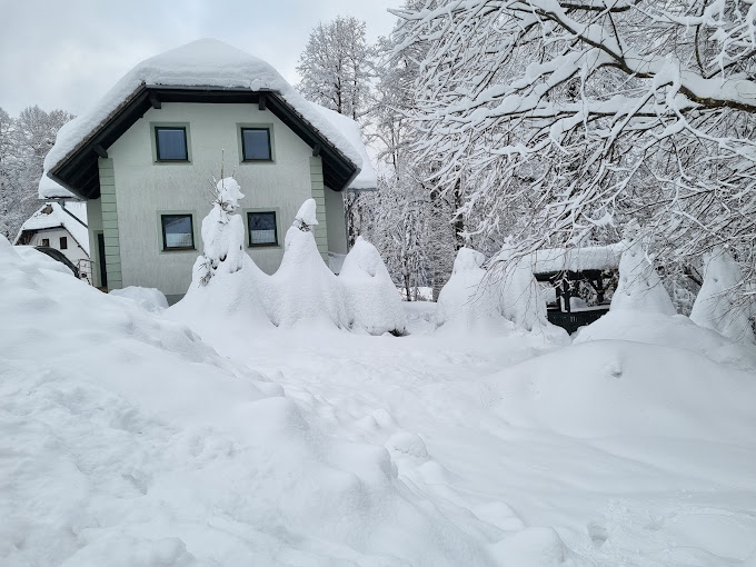 Gače in Slovenia - a house covered in snow with trees in the background.
