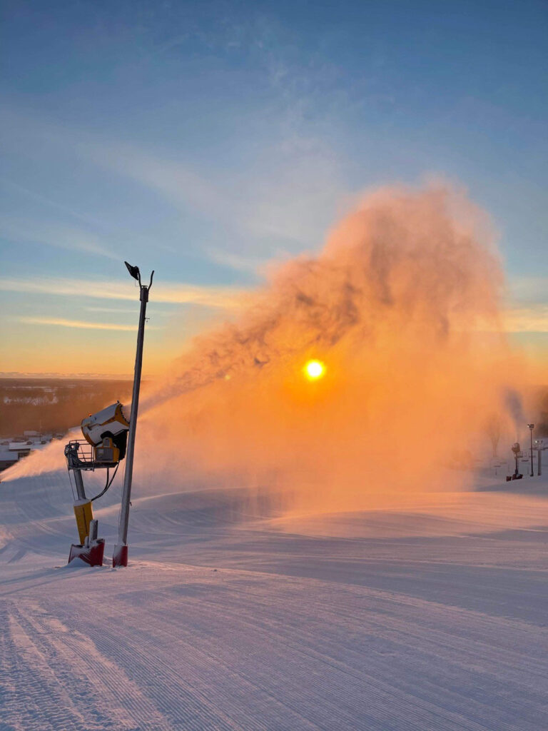 A wintery scene at Wilmot Mountain ski resort in Wisconsin featuring a skier gliding down a snowy slope a distant ski lift and a snowmobile.