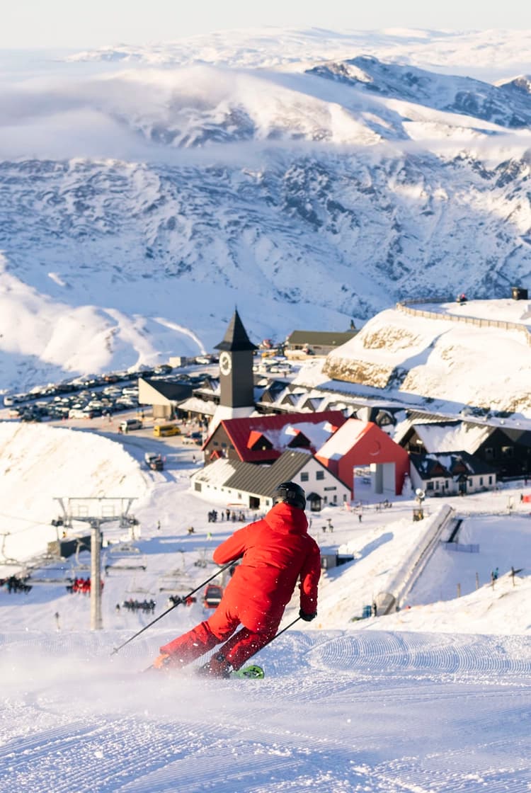 Cardrona in New Zealand - a person in a red jacket skiing down a hill.