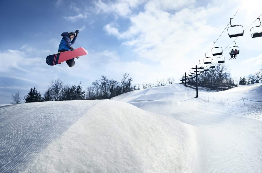 A snowboarder is skillfully carving through the pristine white snow at Seven Oaks in Iowa USA. The surrounding beauty of the snowy landscape enhances the exhilarating atmosphere.