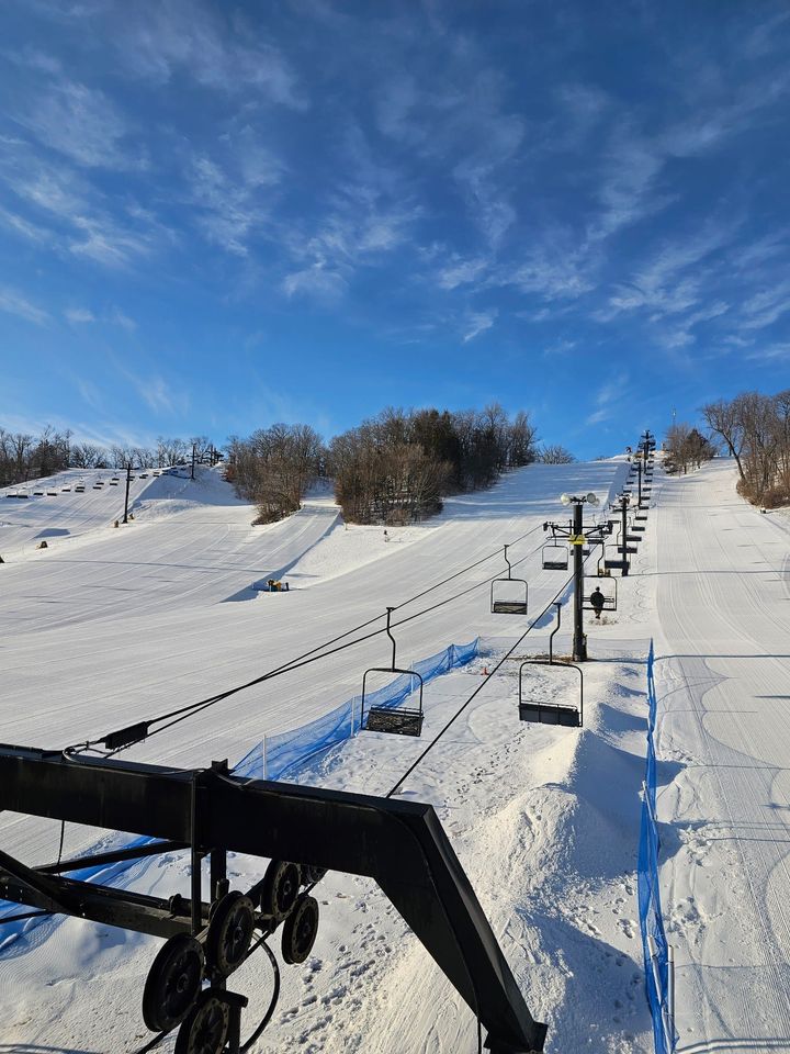 A winter sports scene at Seven Oaks Iowa showcasing a bustling ski resort with a ski lift in the backdrop surrounded by a stunning winter landscape.