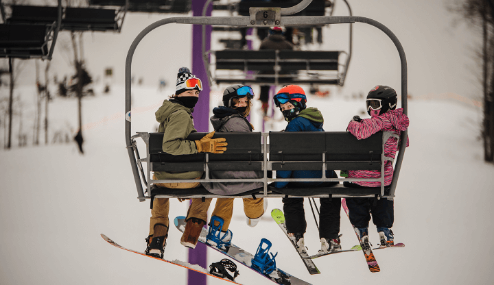 Ski lift operating at Shanty Creek Resorts, Summit Mountain, Michigan with winter sports enthusiasts, including a family and individuals, enjoying a day of skiing.