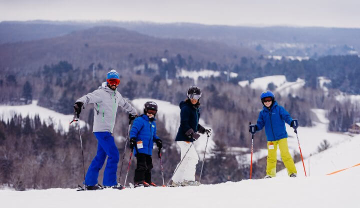 Winter sports scene at Shanty Creek Resorts with groups of people, including families, enjoying skiing at the picturesque Summit Mountain in Michigan, USA.