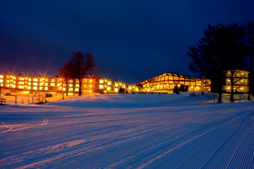 Winter scene at Shanty Creek Resorts – Summit Mountain, Michigan, showcasing a bustling ski resort with visitors engaging in winter sports against a backdrop of a charming chalet and picturesque snowy landscape.