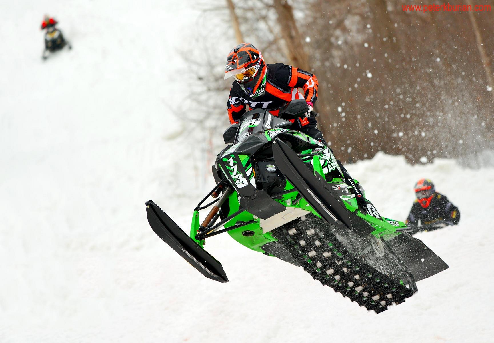 A lively winter sports scene in Chicopee Southern Ontario featuring a snowmobile as the prominent subject with faint impressions of a skier and a snowboarder. A chalet is seen in the backdrop.