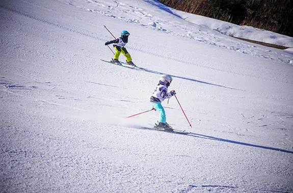 Winter sports scene at Holiday Mountain in The Catskills, NY featuring a skier and a family enjoying their time in the snow, with a child learning to ski near a cozy challet.