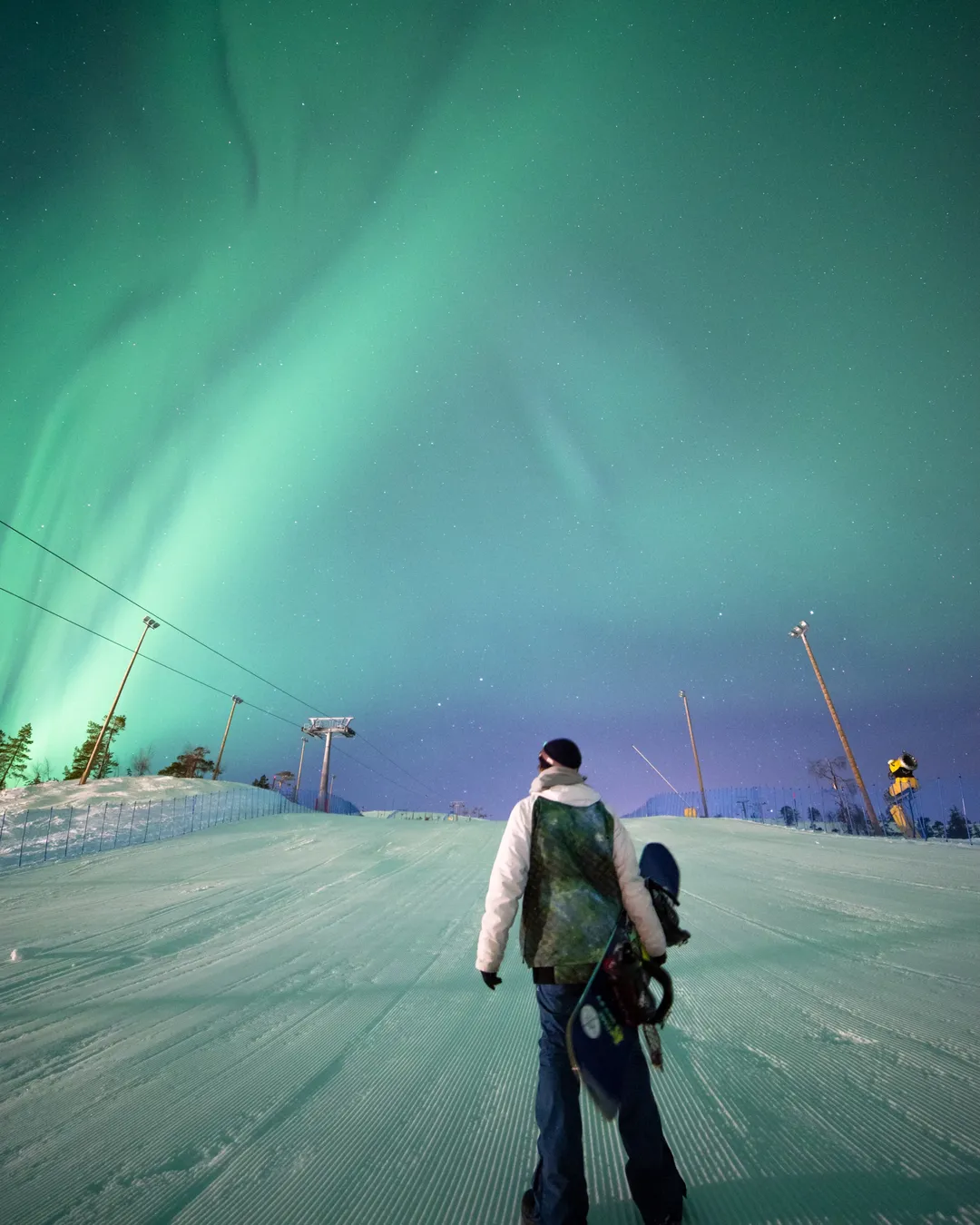 Pyhä in Finland - a man walking down a snow covered slope under the northern lights.