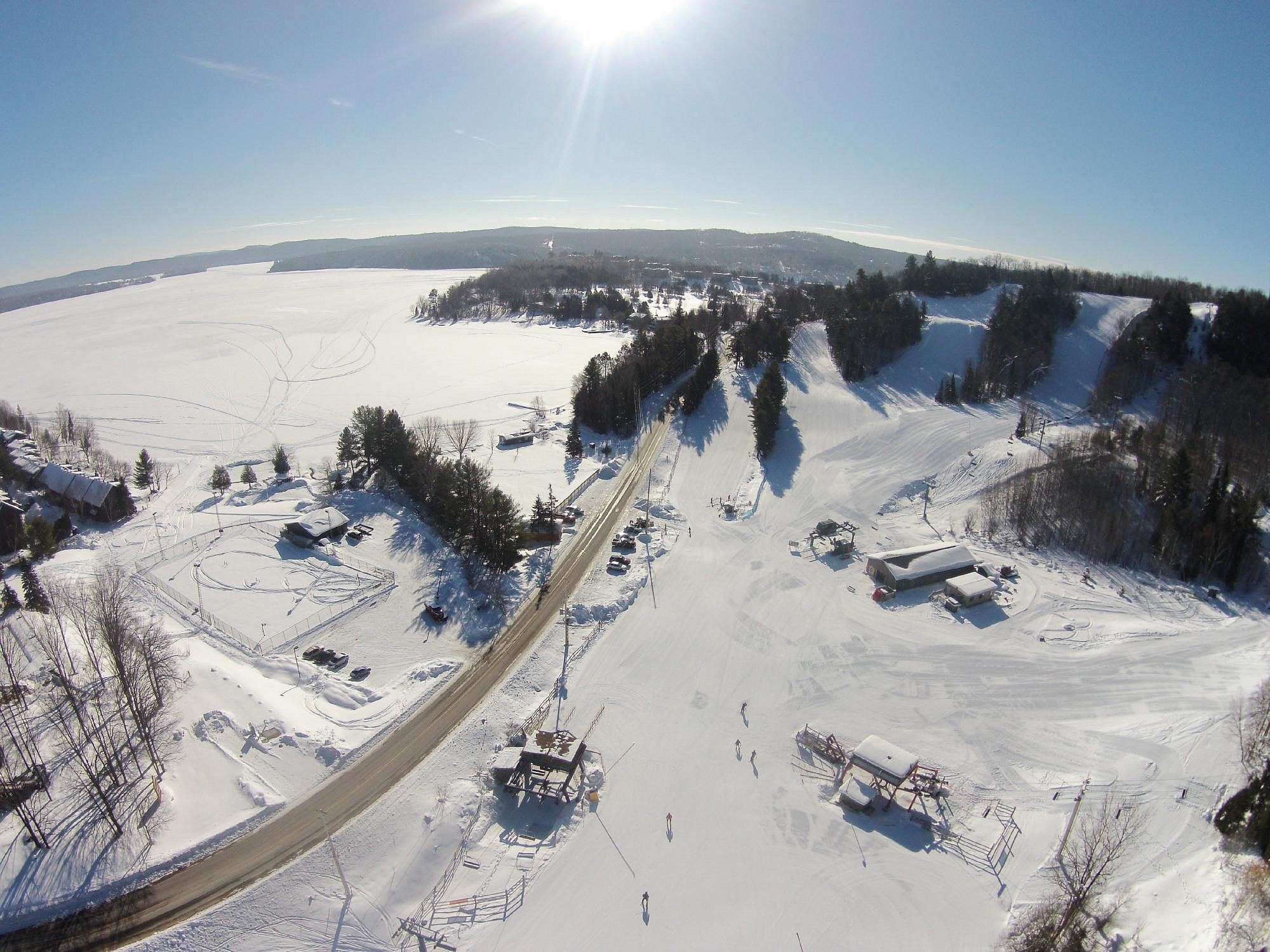 A lively winter sports scene at Hidden Valley Highlands Northern Ontario with skiers and snowboarders enjoying the snow-covered slopes. A chalet sits in the background amidst the beautiful winter scenery.