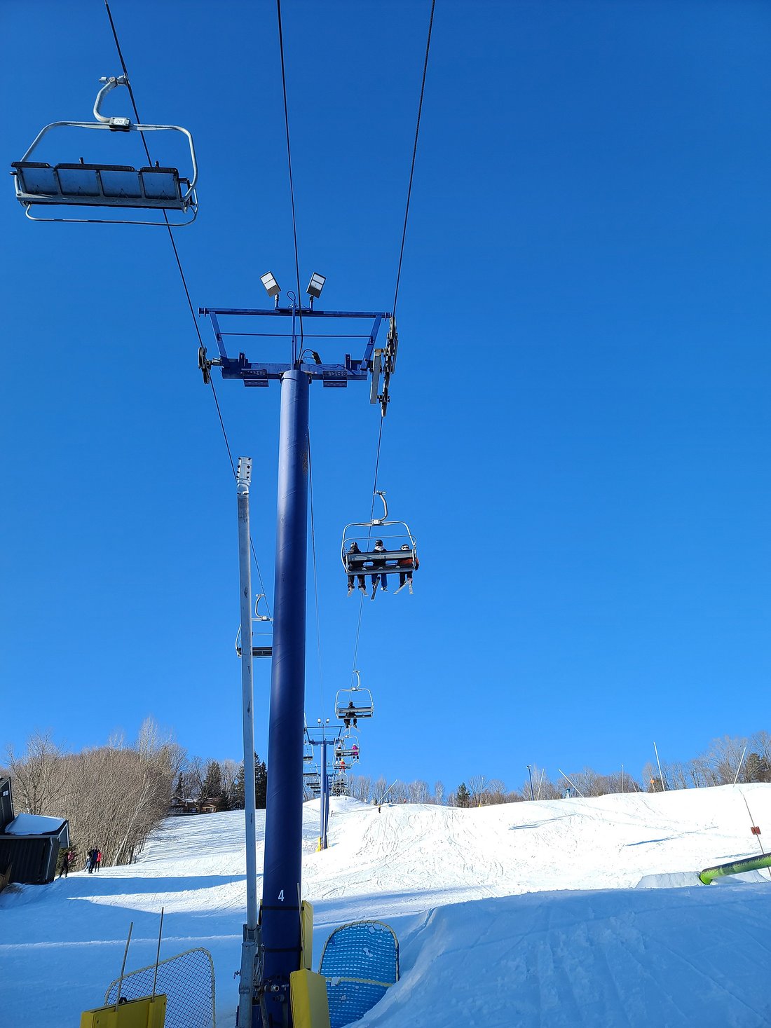 Image of a ski lift amidst the snowy landscape of Hidden Valley Highlands, Northern Ontario, Canada. A skier can be spotted in distance, creating a lively winter sports scene.