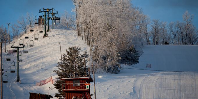 A ski lift operating amidst a winter sports scene at Mt Ashwabay – Salmo ski resort in Wisconsin, featuring stunning winter scenery including a charming chalet.