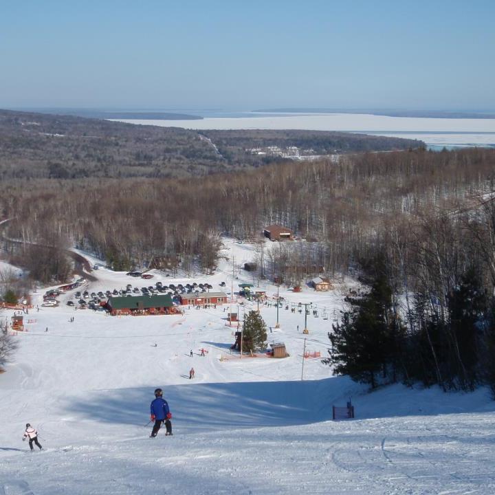A winter sports scene at Mt Ashwabay – Salmo ski resort in Wisconsin, USA, featuring a skier riding the ski lift at the bustling winter sports centre.