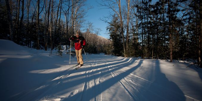 An engaging winter scene at Mt Ashwabay in Wisconsin, USA, highlighting a skier sliding down the slope, potentially with family, amidst well-facilitated surroundings, including a chalet nearby.