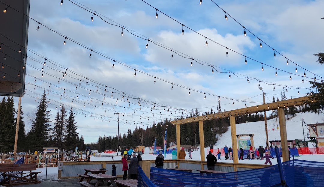 Winter sports scene at Hilltop – Anchorage in Alaska, USA, featuring a bustling ski resort amidst beautiful winter scenery, including a cozy chalet in the distance.