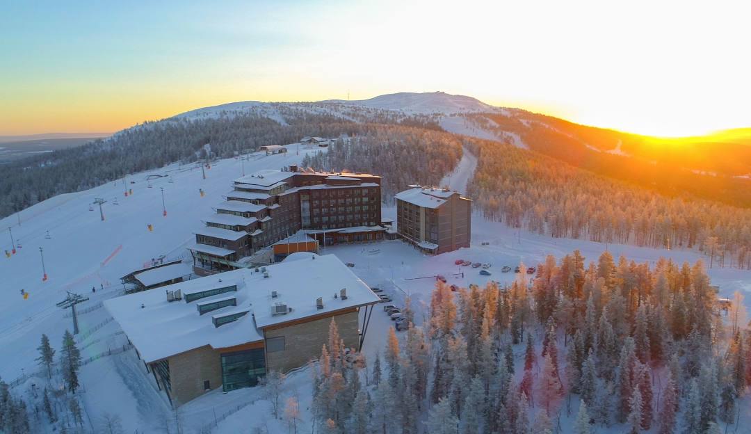 Snow blankets the slopes at the Hilltop Ski Resort in Anchorage, Alaska. A winter sports center outlines the bottom of the frosty hill. Athletes dot the landscape, embracing the active, snowy scene.