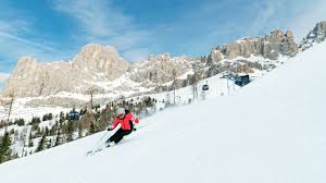 A skier gliding down the snowy slopes of Carezza Dolomites in South Tyrol Italy with a cozy chalet and bustling ski resort visible in the backdrop of this vibrant winter sports scene.