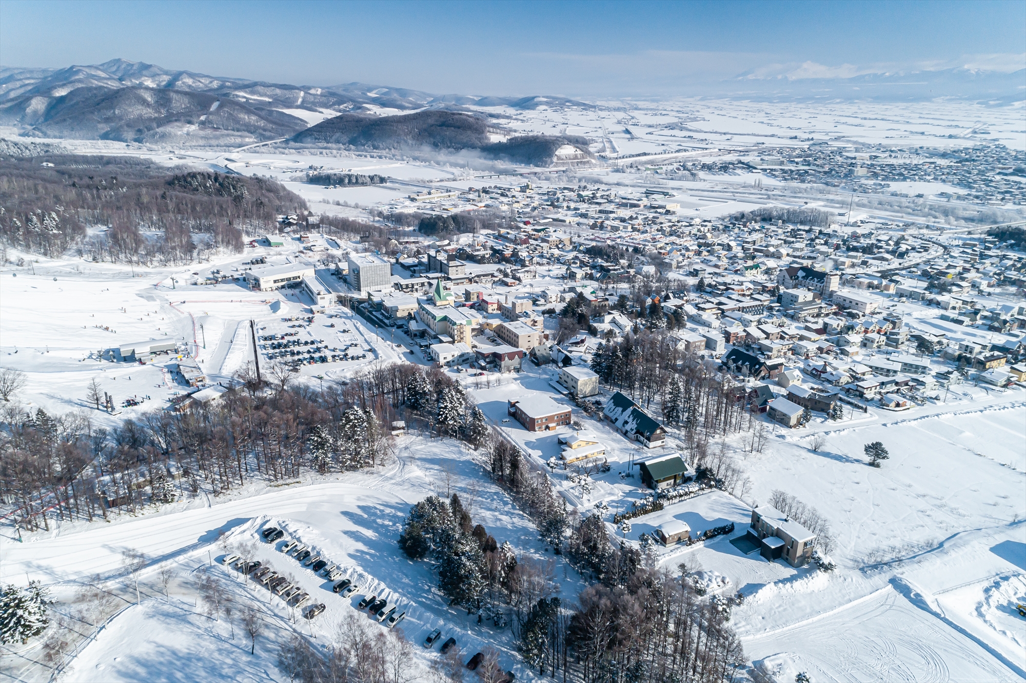 Winter view of Furano, Hokkaido, Japan, showcasing a bustling ski resort amidst stunning snow-covered landscapes, exemplifying an active winter sports scene.