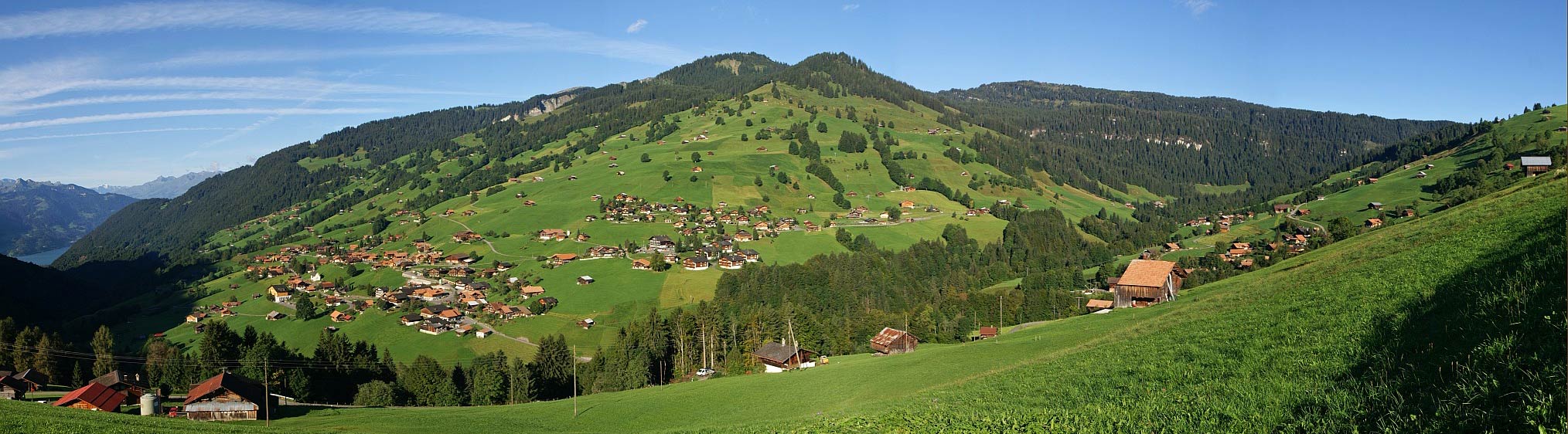 Habkern – Sattelegg in Switzerland - a green hillside with houses and mountains in the background.