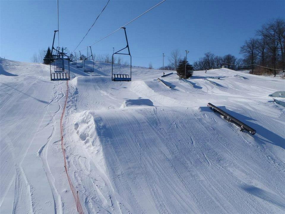 A skier enjoys a winter day at Powder Ridge Ski Resort in Minnesota USA. He's making his way down the slopes powder flying up around him. Nearby a chairlift carries more winter sports enthusiasts to the top.
