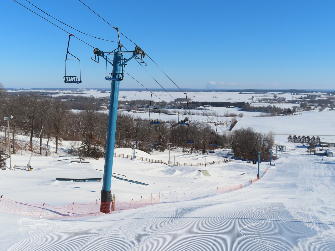 A vibrant winter vista at Powder Ridge in Minnesota featuring a ski lift carrying enthusiastic skiers up the hill and a charming chalet in the background.