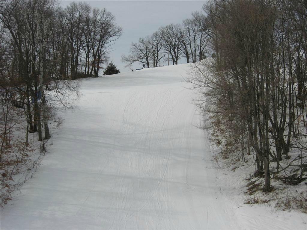 A skier gliding down snow-covered slopes at Powder Ridge, Minnesota. Visible elements include a ski resort with a lift, adding to the winter sports scene.