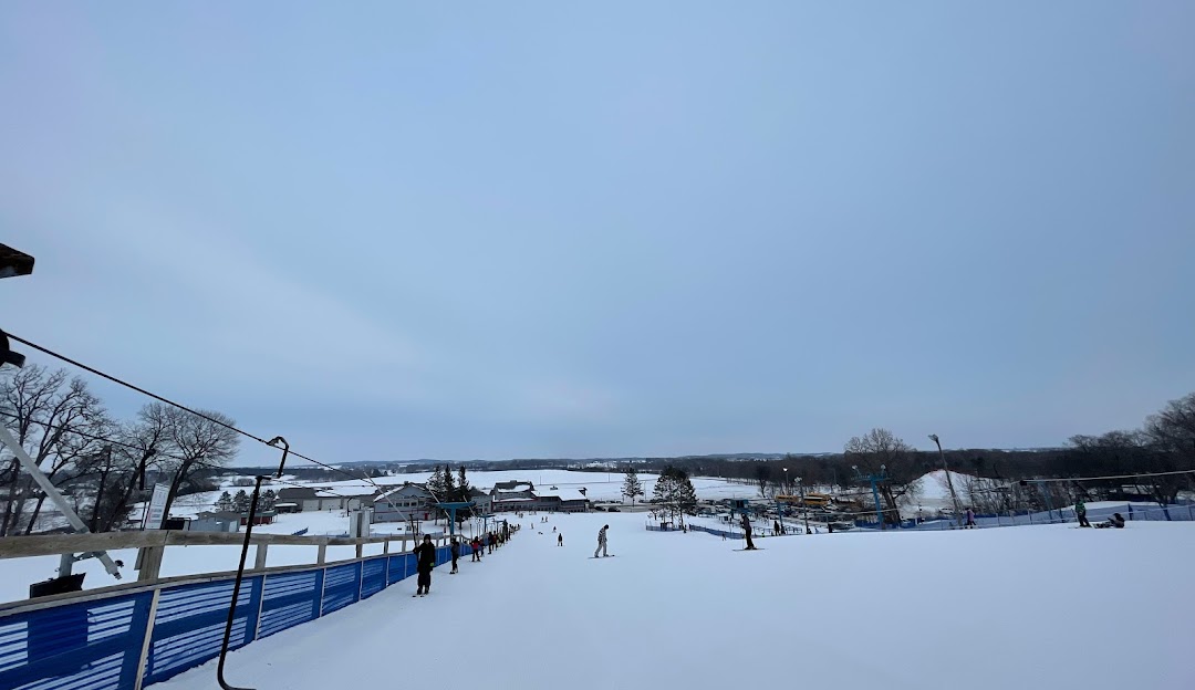 Winter scene at Powder Ridge, Minnesota, showcasing a bustling winter sports centre amidst a beautiful snowy landscape with a ski resort and chalet in the distance.
