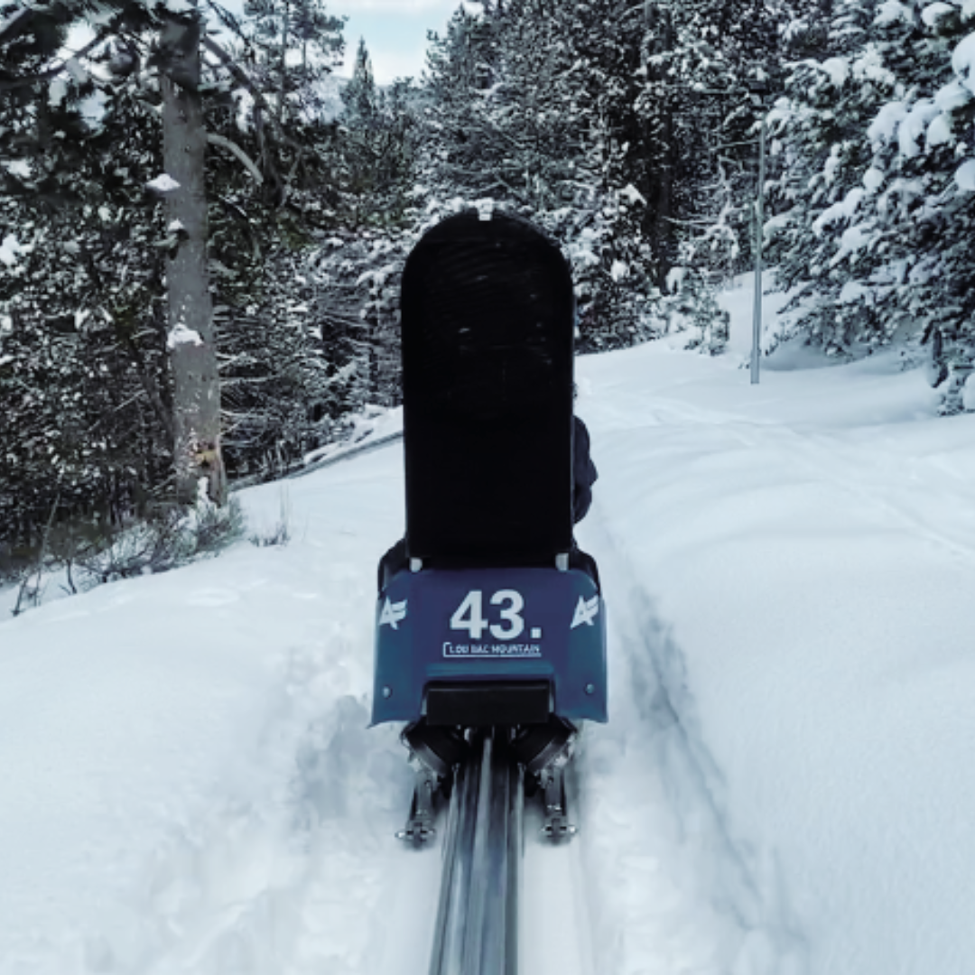 A snowmobile is a prominent feature in the winter sports scene in Les Angles France. A skier can also be seen nearby with a challet and a ski lift close by amidst the snowy landscape.