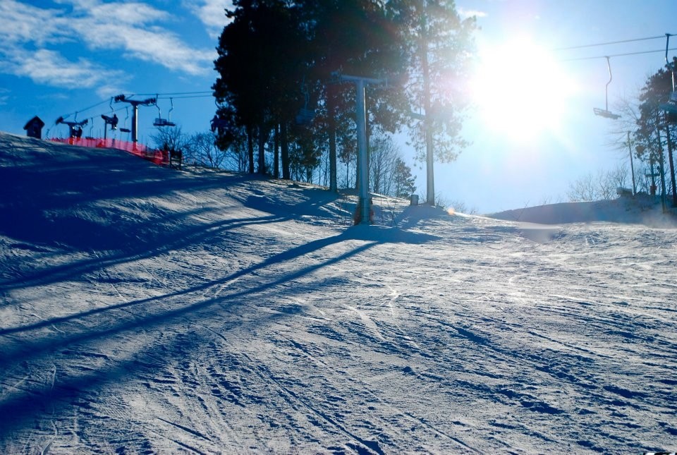 A skier gliding down a snowy slope at Mt Holiday in Michigan with a ski resort a chalet and a ski lift visible against the winter landscape.