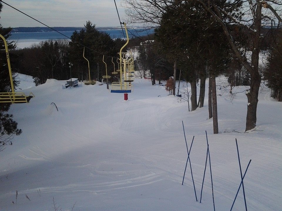 A picturesque winter scene at Mt Holiday Michigan with bustling activity around a ski lift a chalet standing quaintly amidst the snow-covered slopes of a ski resort hinting at a vibrant winter sports community.