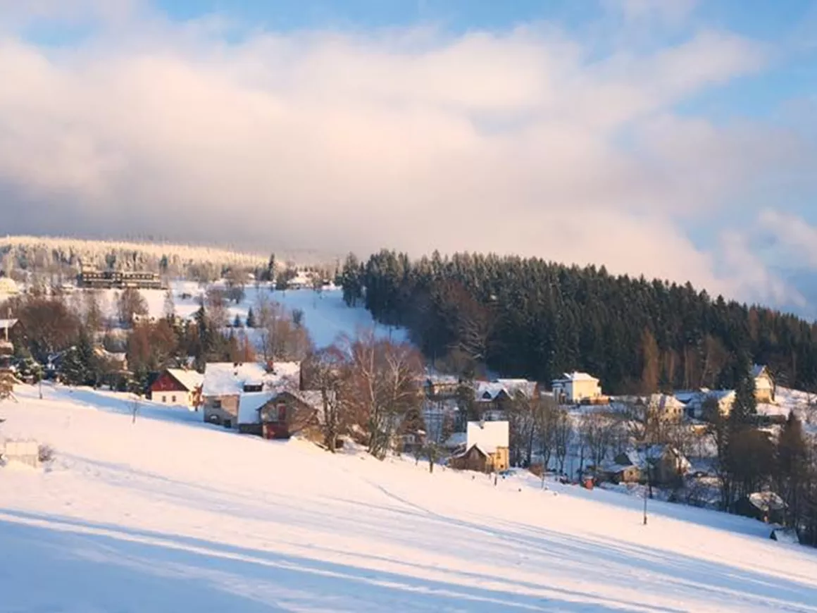 Benecko in Czech Republic - a snow covered mountain with houses and trees in the background.