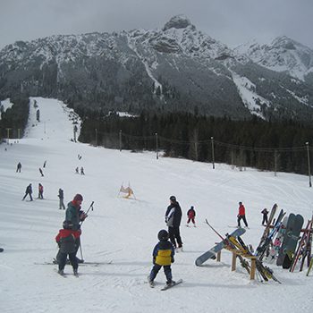 Winter scene at Wapiti Ski Hill in Elkford, British Columbia, featuring skiers enjoying the slopes, with a visible ski lift against the stunning backdrop of the Kootenay Rockies.