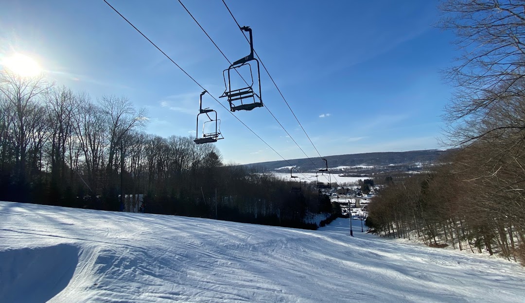 Winter sports scene at Woods Valley in New York, featuring a ski lift transporting skiers up the mountain, a ski resort, a chalet nestled amongst the trees, and a skier gliding on the snow-covered slopes.