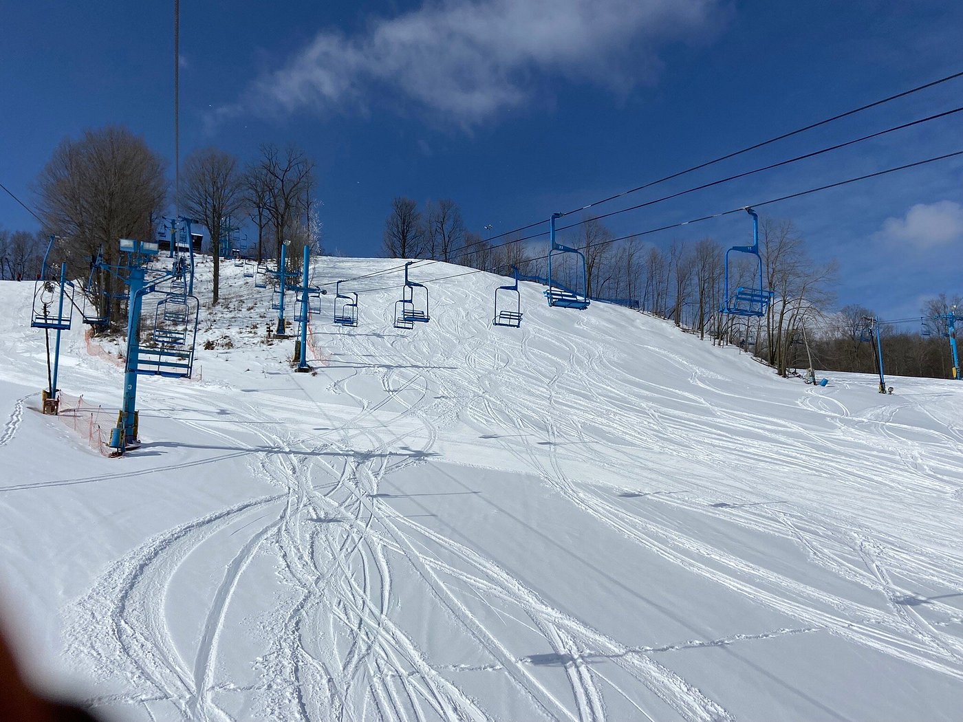 A winter sports scene at Timber Ridge ski resort in Michigan USA featuring a ski lift and a skier. A chalet is visible in the background.