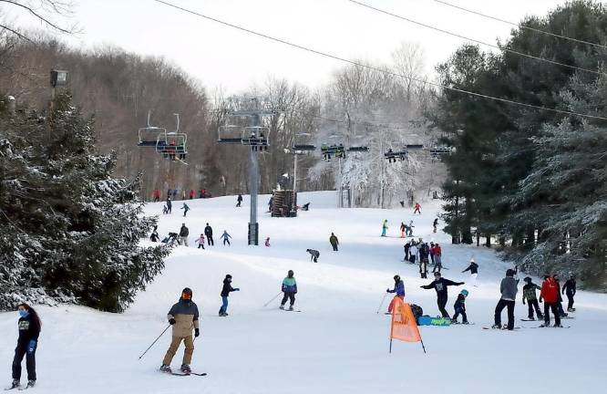 Winter sports enthusiasts enjoying a day on the snow-covered slopes of Mount Peter, Hudson Valley, with a ski lift seen in the background.