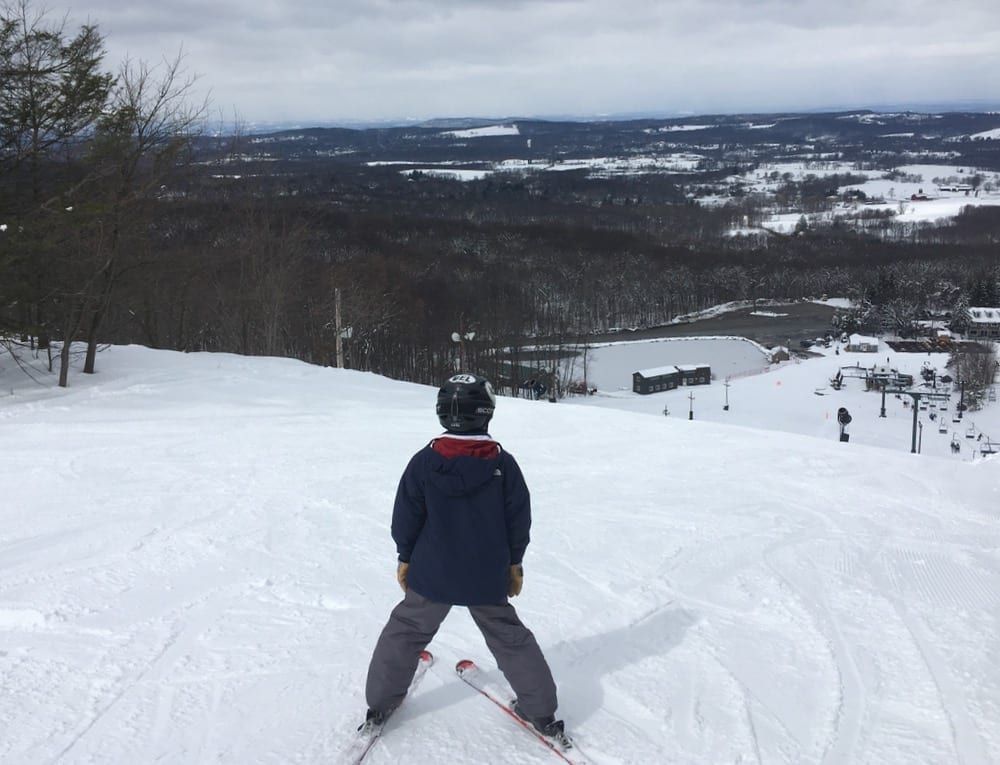 A skier gliding down a snow-covered slope at Mount Peter Ski Resort in Hudson Valley New York with a ski lift visible in the background displaying a typical winter sports scene.