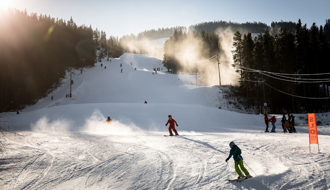 Winter scene at Pass Powderkeg in Southern Alberta, Canada, featuring a ski resort bustling with various activities. Skiers, both individuals and groups, can be seen enjoying their day on the slopes.