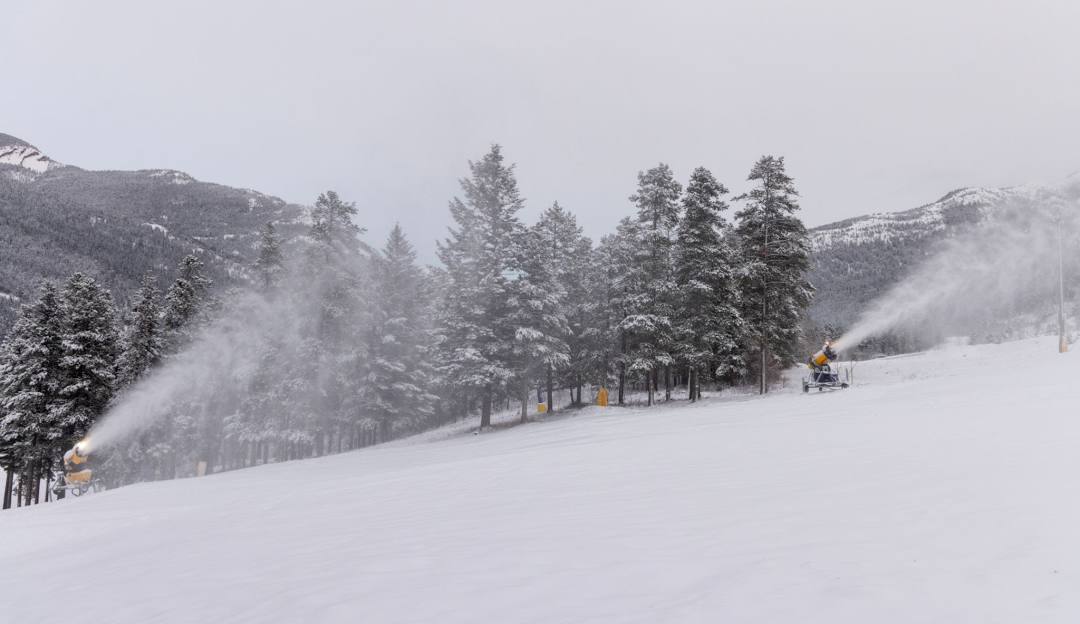 Winter scene at Pass Powderkeg in Crowsnest Pass, Alberta, featuring a bustling ski resort amidst stunning winter scenery. Skiers are using the ski lift under a cloudless sky.