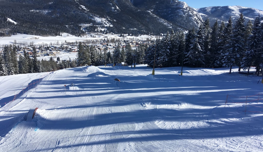 A skier navigating through the snow-covered slopes at Pass Powderkeg ski resort in Southern Alberta, Canada. The winter sports scene includes a chalet in the background.