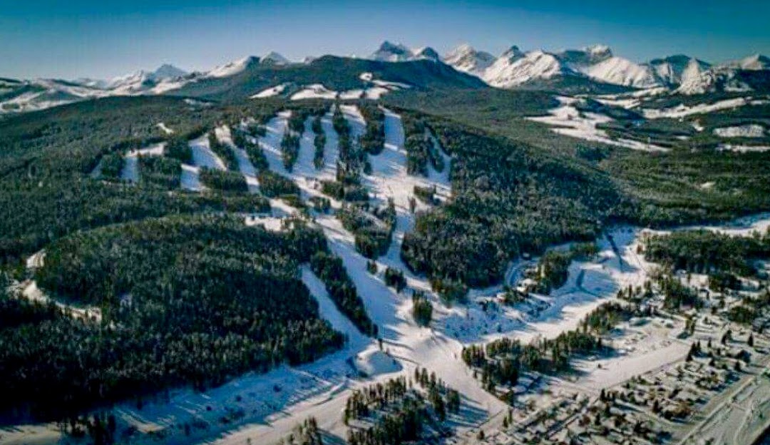 View of Pass Powderkeg ski resort in Southern Alberta, Canada, showcasing snow-covered slopes, a winter sports scene, a chalet, and a mountain backdrop.