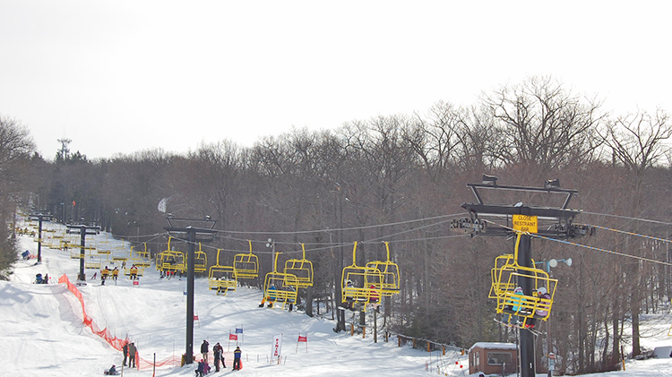 A winter scene at Victor Constant – West Point in New York showcasing a ski lift multiple skiers and a ski resort nestled amidst the snow-covered slopes of Hudson Valley.
