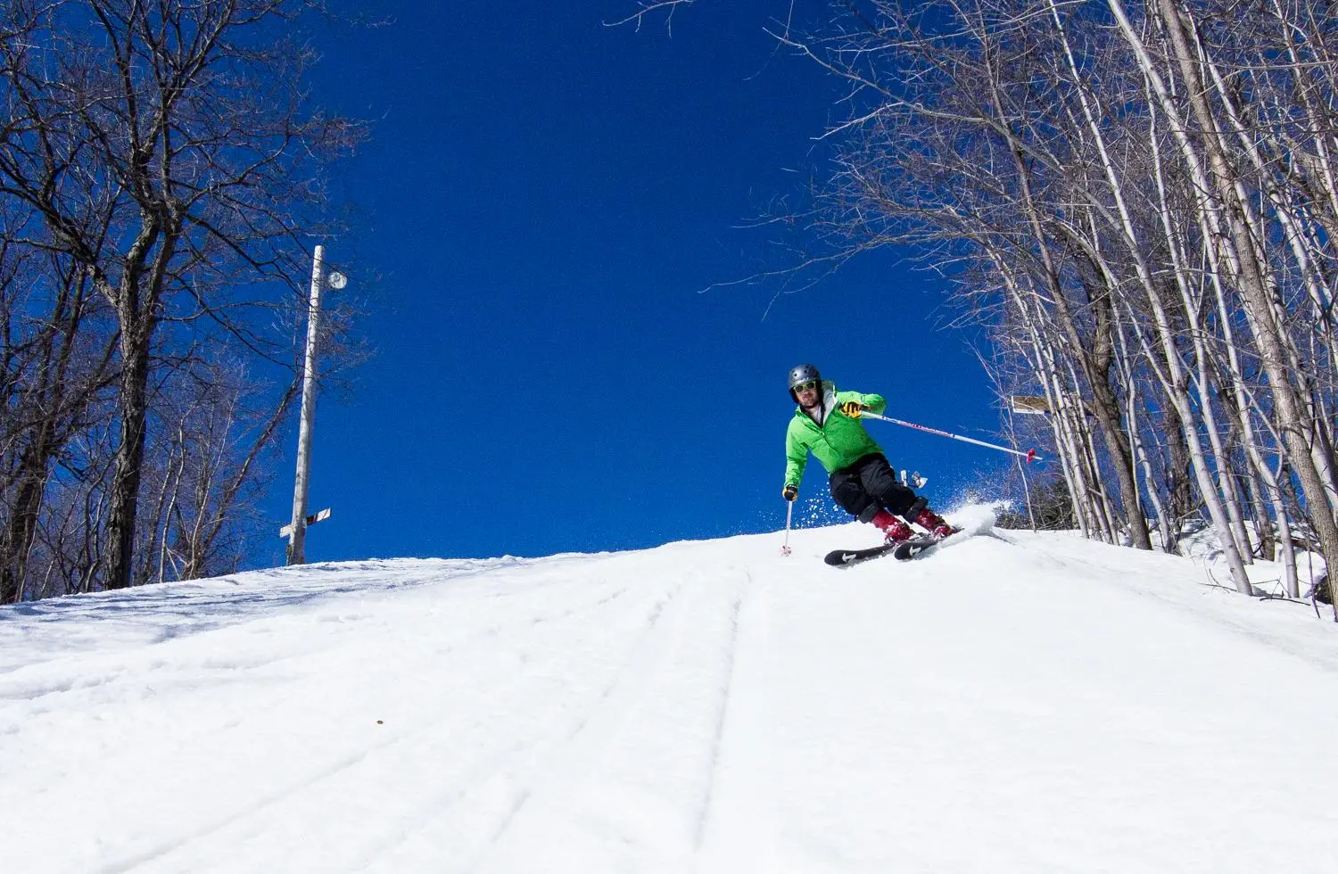 A skier making their way down a snow-covered slope at Little Switzerland, Wisconsin. A ski lift can be seen slightly in the background and a fellow snowboarder is nearby.