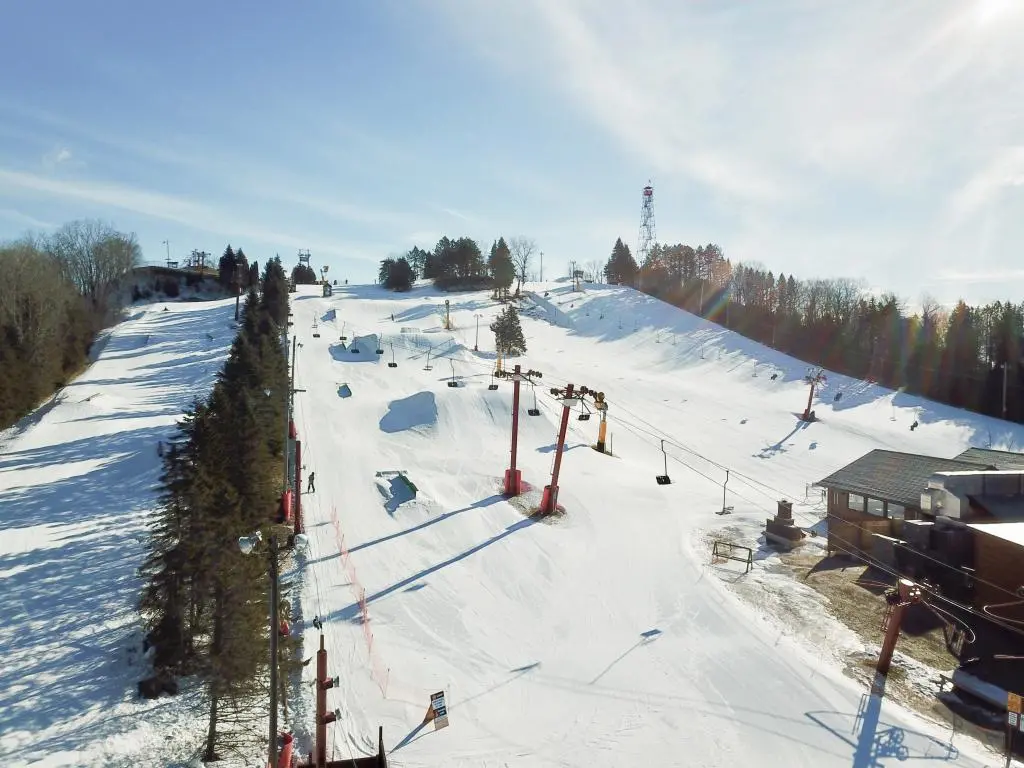 A vibrant winter sports scene at Little Switzerland Wisconsin displaying a bustling ski resort surrounded by snow. Ski lift and chalet are seen in the backdrop.