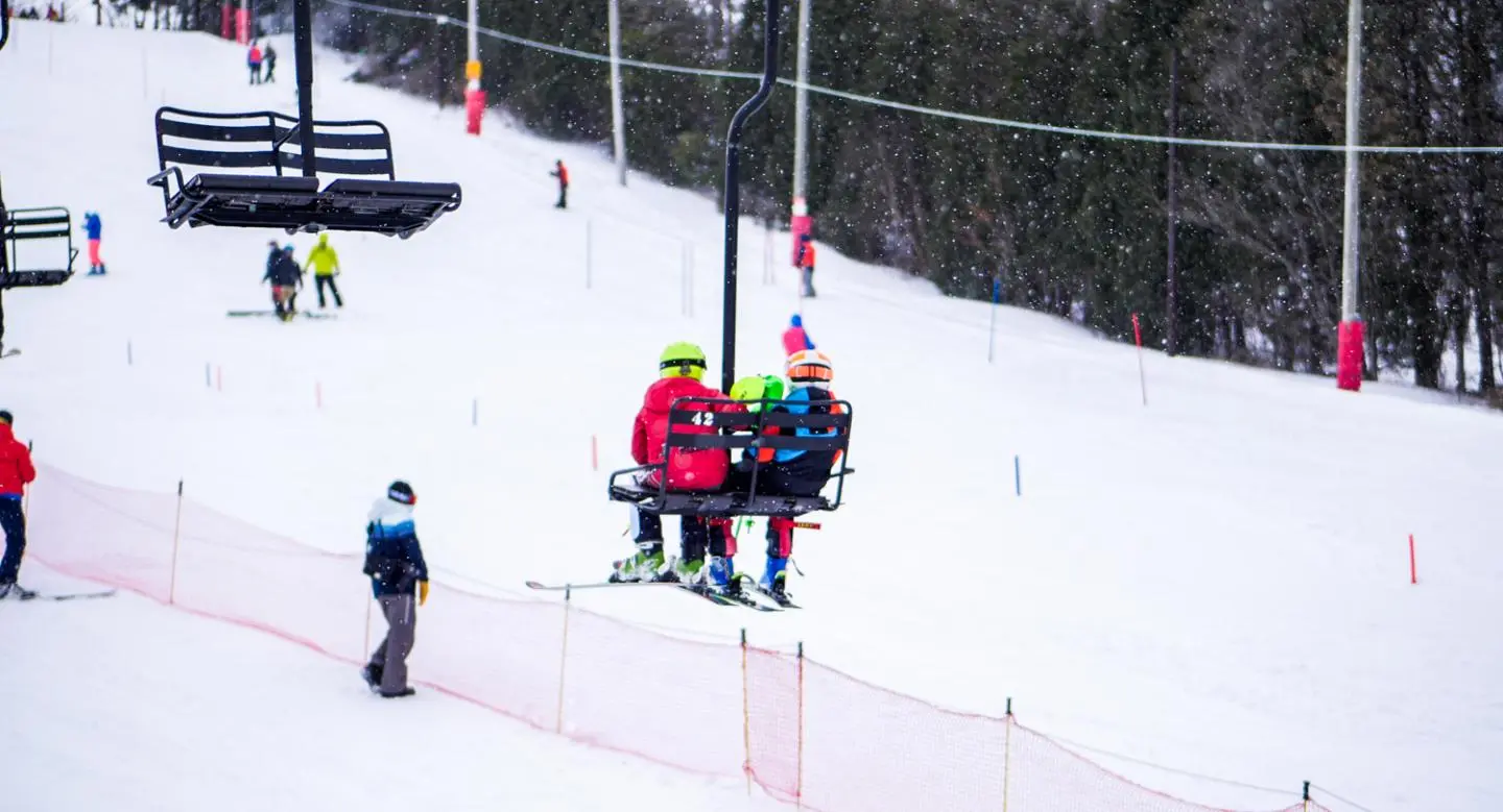 Winter scene at Little Switzerland, Wisconsin, showcasing a busy ski lift in operation, an exhilarating winter sports scene, and individuals skiing down the slope, enjoying the snowy weather.