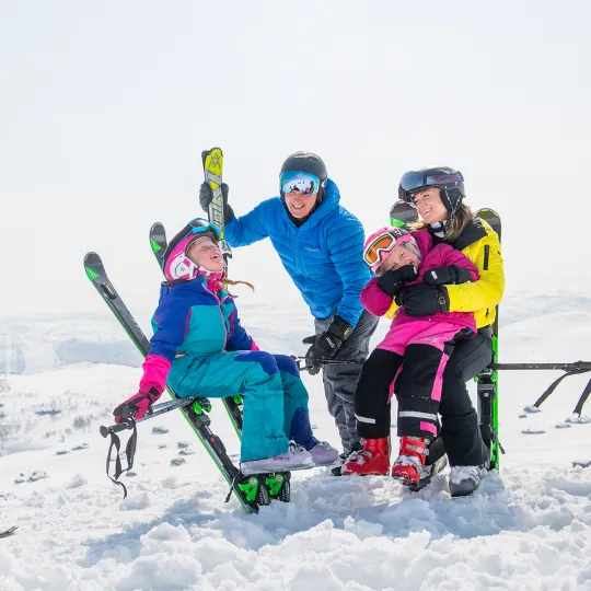 A family enjoy skiing in Geilo, Hallingdal, Norway. The scene captures a vivid winter sports experience, providing glimpses of a ski lift in the background.