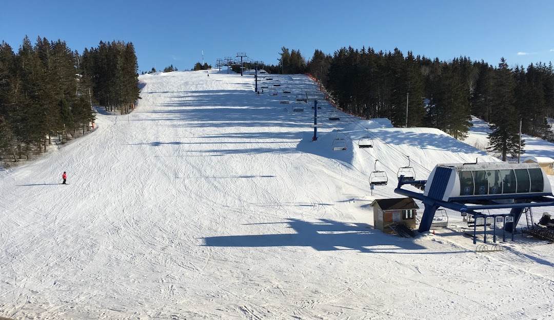 Ski resort at Brookvale Ski Park, Prince Edward Island, showcasing a bustling winter sports scene with a ski lift in operation, and a snowmobile in view.