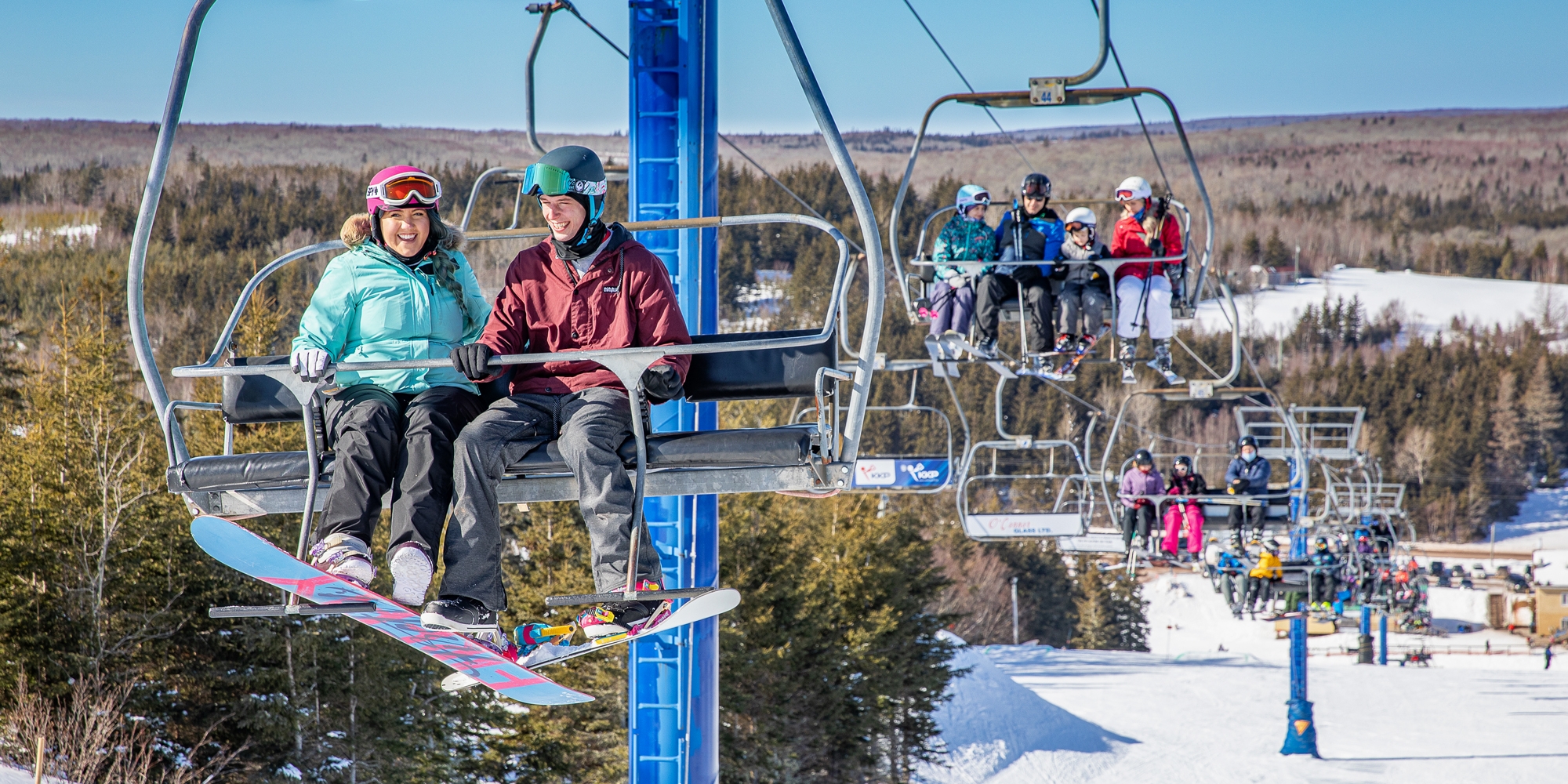 Winter scene at Brookvale Ski Park, PEI, Canada showcasing a busy ski lift and various skiers, including a family, all enjoying the snow-covered slope.