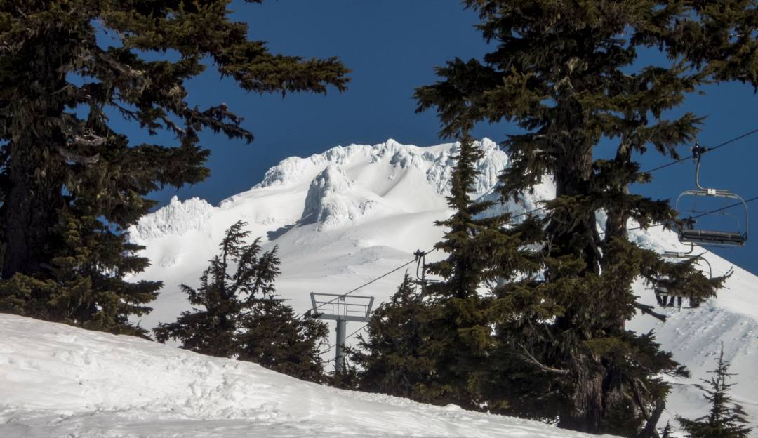 Skier enjoys the breathtaking scenery at Timberline Summit Pass in Oregon, USA. The landscape is dominated by a mountain partially covered in snow, with an emphasis on winter sports activities.